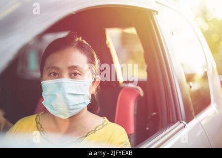 Asiatische Frau trägt schützende Gesichtsmaske und sitzt im privaten Auto. Immer noch Maske auf Reisen zur Vorbeugung der Corona-Virus-Krankheit (COVID- Stockfoto