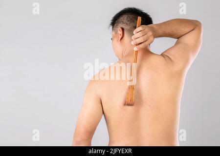 Health Care oder Juckreiz oder Tinea cruris Konzept : Porträt von Menschen mit Scratch Holz Stick Kratzen auf seiner Rückseite. Studio auf grauem Backgro gedreht Stockfoto