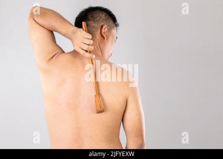 Health Care oder Juckreiz oder Tinea cruris Konzept : Porträt von Menschen mit Scratch Holz Stick Kratzen auf seiner Rückseite. Studio auf grauem Backgro gedreht Stockfoto