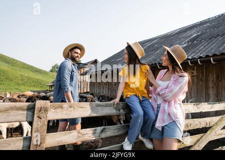 Mädchen im Strohhut sitzt auf einem Holzzaun in der Nähe von Mama und Papa im Corral Stockfoto