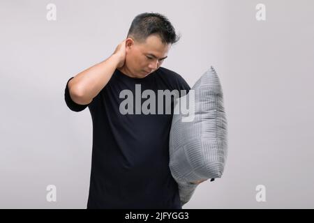 Nackenschmerzen Konzept : Portrait asiatischen Mann hält graue Kissen und fühlen sich müde oder Schmerzen auf seinem Hals. Studioaufnahme isoliert auf grauem Hintergrund Stockfoto