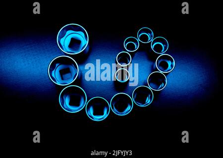 Steckschlüsselköpfe aus Chrom-Vanadium auf dem dunkelkörnigen Hintergrund in neonblauem Licht. Sie sind ein seltsames Symbol. Hintergrundbild. Stockfoto