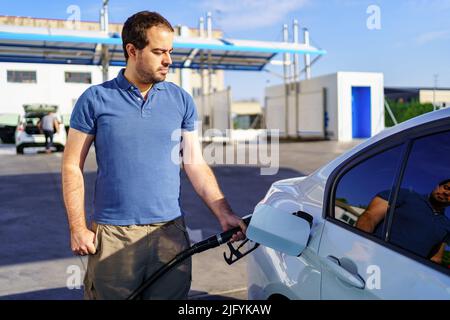 Kaukasischer junger Mann, der den Tank eines Benzinwagens an einer Tankstelle nachfüllt. Stockfoto