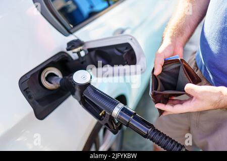 Hände eines Mannes, der die leere Brieftasche zeigt, nachdem er an einer Tankstelle aufgetankt hat. Stockfoto