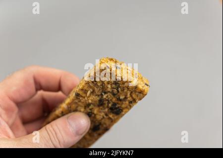 Ein Mann hält Protein Energy Bar in der Hand auf Braun. Ein glutenfreier, zuckerfreier Snack. Haferflocken mit Obst. Gesunde Lebensmittel. Stockfoto