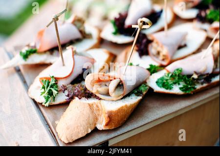 Köstliches Catering-Bankettbuffet im rustikalen Stil im Garten. Verschiedene Snacks, Sandwiches mit Schinken, Grünpflanzen Stockfoto