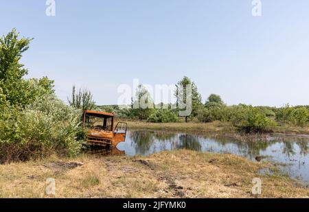 TSCHERNIHIW REG, UKRAINE - 19. Juni 2022: Krieg in der Ukraine. Ein ausgebrannter Bus wird in einem kleinen See aufgegeben. Landschaften der Ukraine nach dem Einmarsch russischer Faschisten Stockfoto