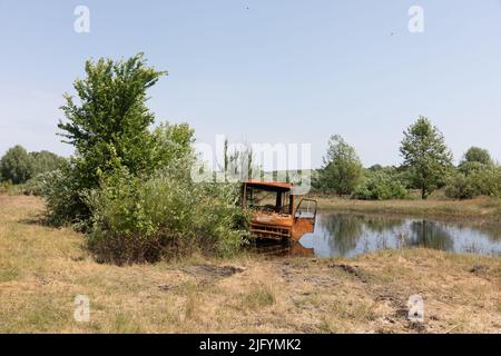 TSCHERNIHIW REG, UKRAINE - 19. Juni 2022: Krieg in der Ukraine. Ein ausgebrannter Bus wird in einem kleinen See aufgegeben. Landschaften der Ukraine nach dem Einmarsch russischer Faschisten Stockfoto