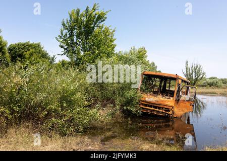 TSCHERNIHIW REG, UKRAINE - 19. Juni 2022: Krieg in der Ukraine. Ein ausgebrannter Bus wird in einem kleinen See aufgegeben. Landschaften der Ukraine nach dem Einmarsch russischer Faschisten Stockfoto