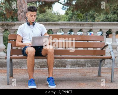 Ein Mann mit Ohrhörer, der mit seinem Laptop in einem öffentlichen Raum studiert Stockfoto