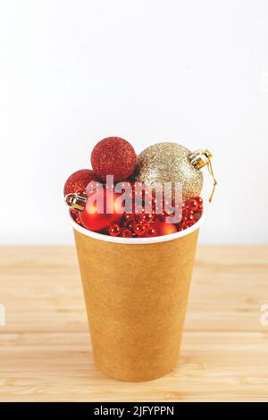 Papierkaffeetasse mit Weihnachtskugeln und Dekorationen an weißen Wänden mit leerem Raum. Vertikaler Neujahrs-Hintergrund mit Kopierbereich. Stockfoto