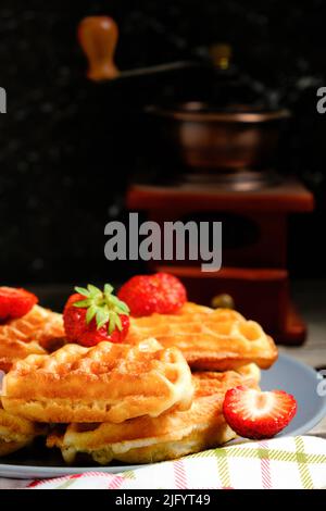Waffeln mit Erdbeeren und Honig, süßes Gebäck auf dem Teller, vor dem Hintergrund Kaffeemühle Stockfoto