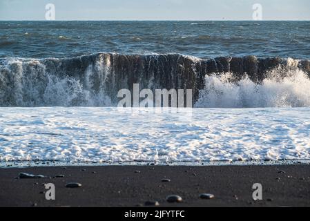 Mächtige Meereswelle rollt auf den schwarzen Lavasand des berühmten Reynisfjara-Strandes in Island zu Stockfoto