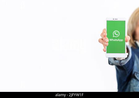 Glückliche Frau auf weißem Hintergrund mit einem Smartphone mit whatsapp-Logo auf dem Bildschirm. ROSARIO, ARGENTINIEN - 22. OKTOBER 2021 Stockfoto