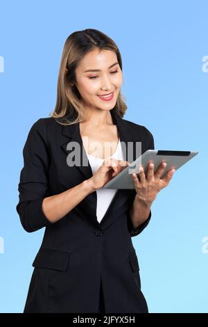 Studioaufnahme einer Geschäftsfrau in schwarzem Anzug, die auf digitalem Teeblet auf blauem Hintergrund arbeitet. Stockfoto