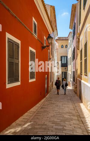 Blick auf ein Paar, das durch eine pastellfarbene Straße in der Altstadt geht, Ciutadella, Menorca, Balearen, Spanien, Mittelmeer, Europa Stockfoto