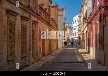 Blick auf ein Paar, das durch eine pastellfarbene Straße in der Altstadt geht, Ciutadella, Menorca, Balearen, Spanien, Mittelmeer, Europa Stockfoto