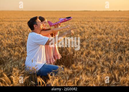 Nettes Mädchen spielt mit Spielzeug Flugzeug gegen Himmel im Weizenfeld Stockfoto