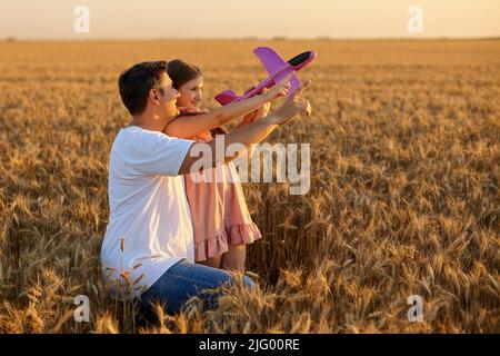Nettes Mädchen spielt mit Spielzeug Flugzeug gegen Himmel im Weizenfeld Stockfoto