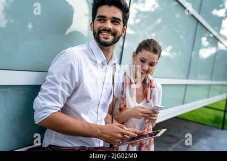Glückliche junge Geschäftsleute, die im Freien chatten und digitale Geräte nutzen Stockfoto