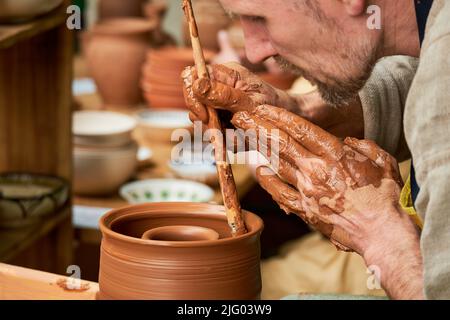 Ein Mann in mittelalterlicher Kleidung sitzt hinter einem alten Töpferrad und macht Geschirr aus Ton. Times and Epochs Festival auf den Straßen von Moskau, Russland, Stockfoto