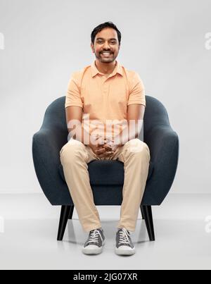 Glücklich lächelnder junger indischer Mann, der auf einem Stuhl sitzt Stockfoto
