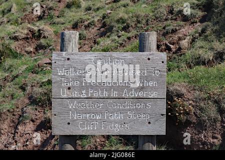 Holzschild warnt Wanderer, bei schlechtem Wetter auf rutschige Bedingungen zu achten Stockfoto