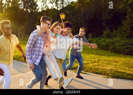 Lustige beste Freunde, die Spaß haben, am warmen Sommertag auf dem Bürgersteig im öffentlichen Stadtpark zu laufen. Stockfoto