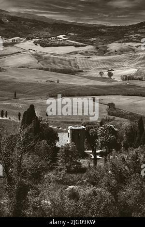 Toskana, Italien. Val d'Orcia malerische Hügellandschaft mit blühenden Rapsblumen und antikem Bauernhaus aus Stein mit Turm. Sepia Stockfoto