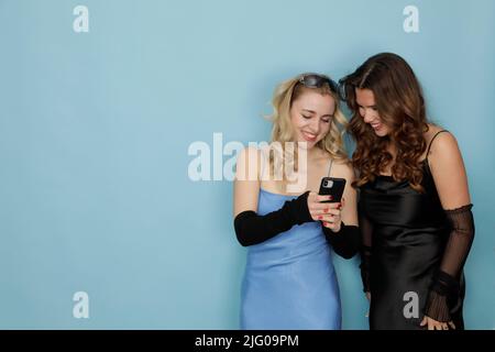 Zwei junge schöne Frauen, lachend und Blick in ihre Handys isoliert vor einem hellen Hintergrund | HEADER, BANNER, COPY SPACE Stockfoto