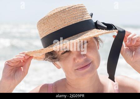 Porträt einer grauhaarigen Frau in einem Bootsfahrer mit einem schwarzen Band philosophisch nachdenklich etwas mit einem kleinen Lächeln zu beobachten.Konzept der Weiblichkeit. Stockfoto