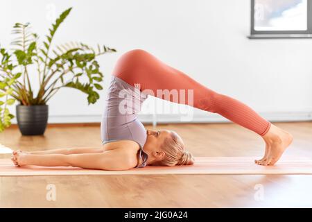 Frau, die zu Hause Yoga in Pflug-Pose macht Stockfoto