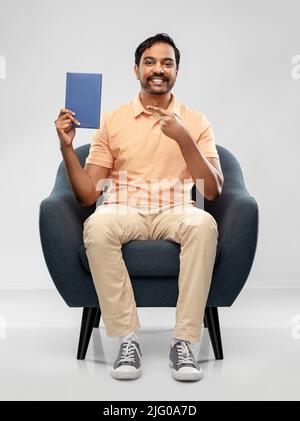 Glücklicher junger indischer Mann, der Buch auf einem Stuhl zeigt Stockfoto