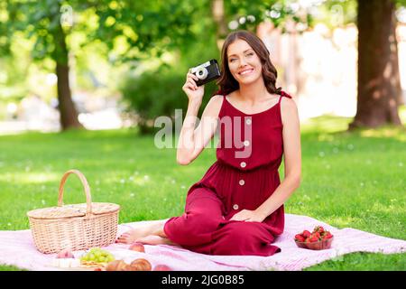 Glückliche Frau mit Kamera beim Picknick im Park Stockfoto