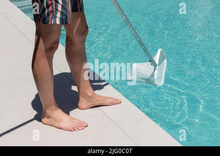 Nahaufnahme eines nicht erkennbaren Mannes, der mit einem Reinigungsnetz die Oberfläche seines Heimoberpools reinigte Stockfoto