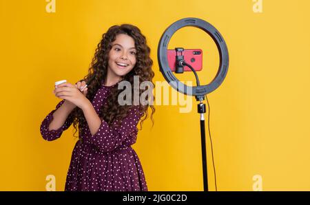 Glückliches Kind mit langen lockigen Haaren macht Video für Blog halten Puderbürste Stockfoto