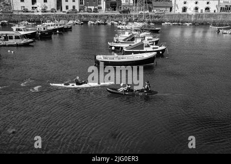 Touristen, die im Innenhafen von Porthleven, Cornwall, Kajakfahren Stockfoto