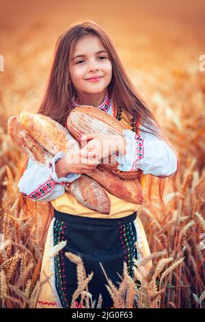 Schöne Mädchen Frau in traditionellen bulgarischen Folklore-Kleid mit hausgemachtem Brot im Weizenfeld Stockfoto