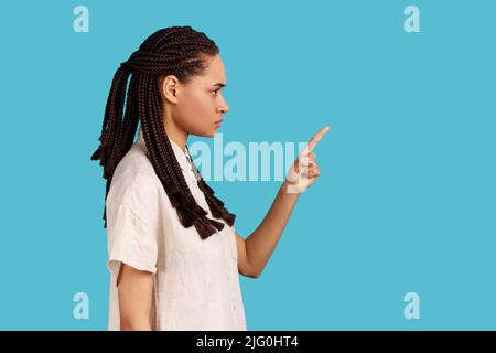 Seitenansicht Porträt einer ernsthaften strengen Frau mit schwarzen Dreadlocks, die den Zeigefinger heben, sieht wütend aus und warnt vor Gefahren. Innenaufnahme des Studios isoliert auf blauem Hintergrund. Stockfoto