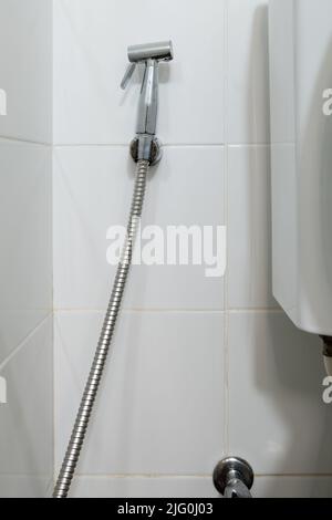 Das Metall-Bidet-Spray hängt an der weißen Fliesenwand in der Nähe der Spültoilette in der Toilette des Stadthauses, sauber und hygienisch für den Benutzer, fron Stockfoto