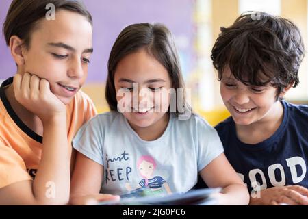 Drei kaukasische Schulkinder haben eine lustige Zeit im Unterricht, während sie zusammen lernen. Nahaufnahme. Stockfoto