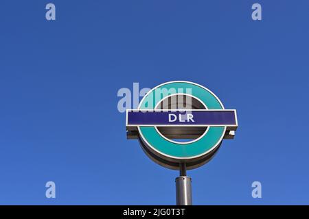 London, England - 2022. Juni: Schild vor dem Eingang zu einem Bahnhof auf der Docklands Light Railway, isoliert vor einem tiefblauen Himmel Stockfoto