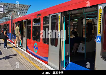 London, England - 2022. Juni: Personen, die an einem Bahnhof mit der Docklands Light Railway in einen Zug einsteigen Stockfoto