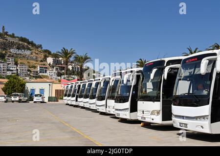 Kusadasi, Türkei - Juni Mai 2022: Reihe von Reisebussen wartet auf Passagiere von einem Kreuzschiff. Im Hintergrund ist ein Schild auf dem Hügel Stockfoto