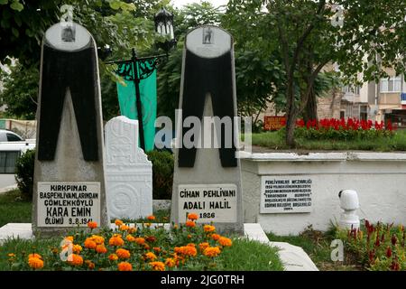 Kırkpınar (Türkisches Ölwrestling). Gräber von Kırkpınar-Ringern auf dem Ringfriedhof im Stadtzentrum von Edirne, Türkei. Die Kırkpınar-Wrestlerin Kara Emin (gestorben 1941), die 1926 das Kırkpınar-Turnier gewann, und die Kırkpınar-Wrestlerin Adalı Halil (1870-1927) sind im Vordergrund unter den Grabsteinen in Form einer traditionellen schwarzen Lederhose namens Kisbet begraben. Stockfoto