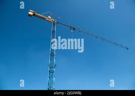 Bau eines Gebäudes: Der Turmdrehkran mit seinem Haken transportiert tonnenweise Material von einem Stockwerk zum anderen innerhalb der Baustelle. Stockfoto