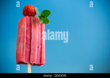 Gekochtes hausgemachtes Erdbeereis auf einem Stock, isoliert auf blauem Hintergrund Stockfoto