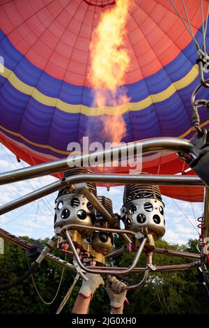 Ein Heißluftballon. Orangefarbene Flammen feuern in die Ballonhülle, um sie mit heißer Luft zu füllen. Stockfoto
