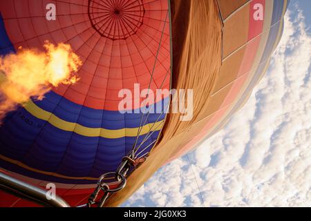 Ein Heißluftballon. Orangefarbene Flammen feuern in die Ballonhülle, um sie mit heißer Luft zu füllen. Stockfoto