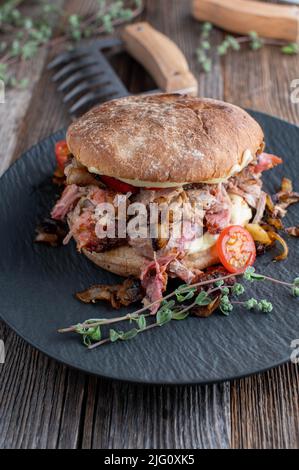 Burger mit Schweinefleisch, Käse, Tomaten und gebratenen Zwiebeln auf Holztisch Stockfoto